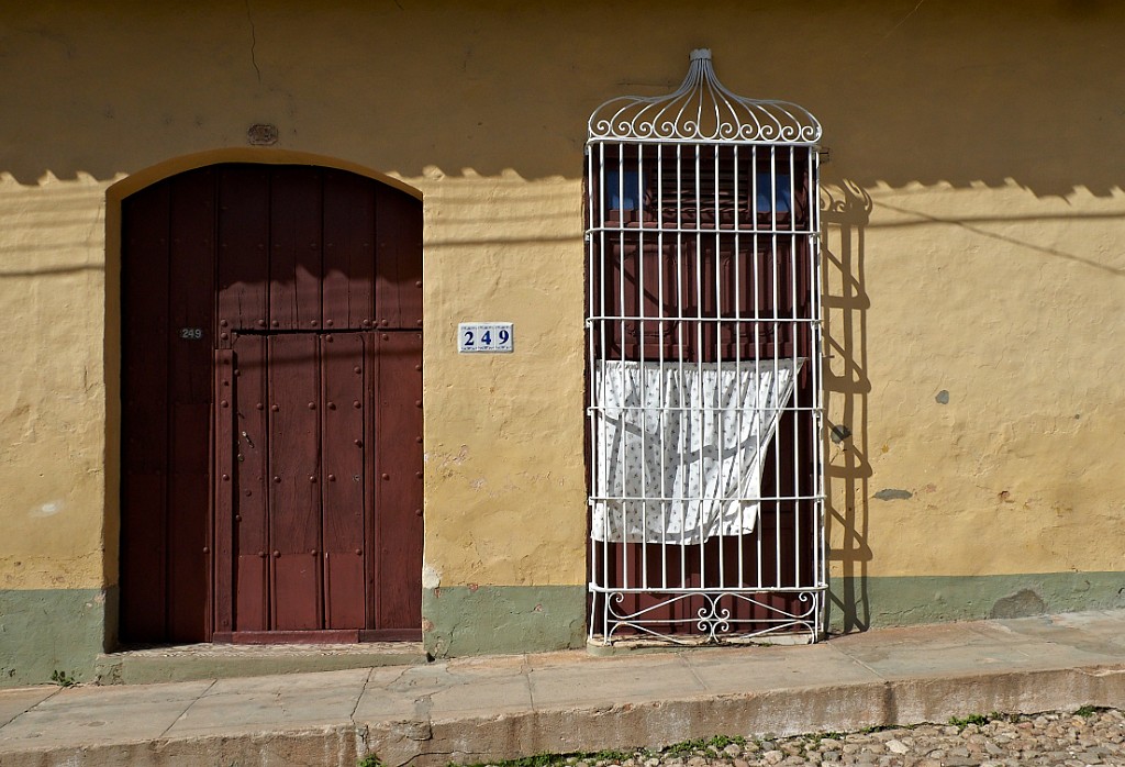 Maisons coloniales toutes disposées en carré avec cour intérieure, porte centrale percée d'une plus petite et fenêtres sans vitres protégées par des volets et des grilles de fer forgé